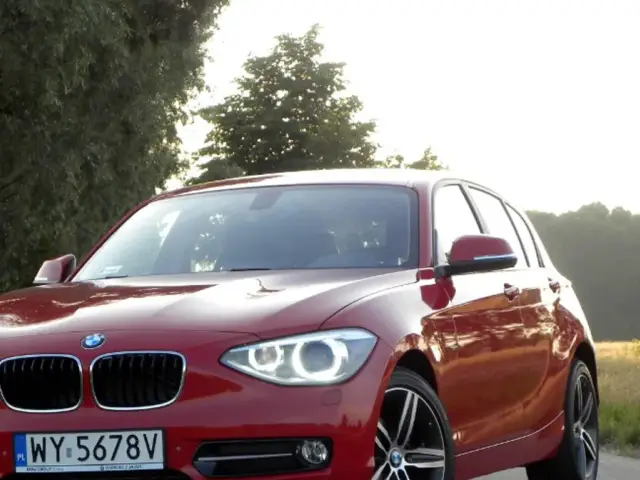 Czerwone BMW 118d na tle drzew i pól.