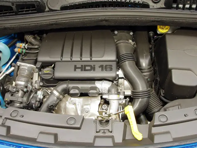 Silnik HDI 16 w Citroenie C4. Widoczny jest czarny plastikowy dekiel z napisem "HDI 16", przewody, rury dolotowe i inne elementy jednostki napędowej.