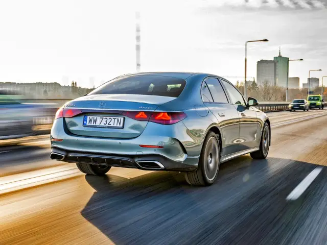 Elegancki, błękitny Mercedes E220d 4MATIC pędzi autostradą, mijając miejską panoramę.