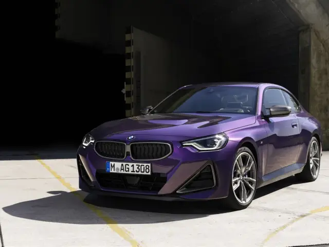 Fioletowe BMW 220i coupe z nowoczesnym designem, zaparkowane na betonowym placu przed ciemnym budynkiem.