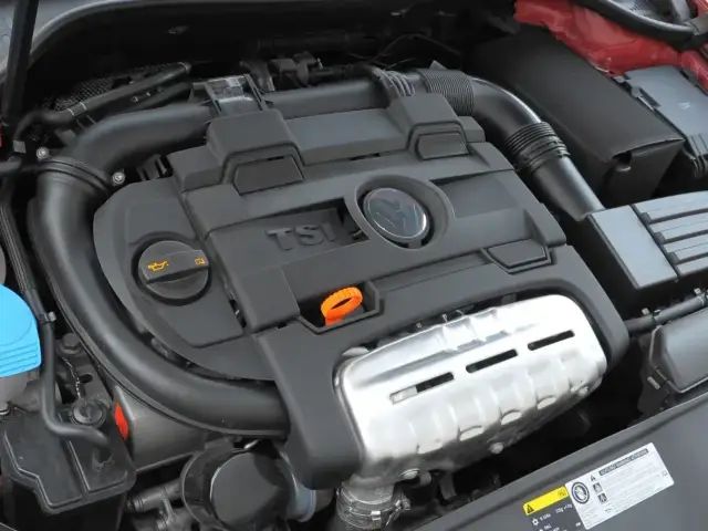 Silnik 1.4 TSI z widocznym logo VW. Czarna pokrywa silnika z napisem TSI i pomarańczową pętlą do sprawdzania oleju.
