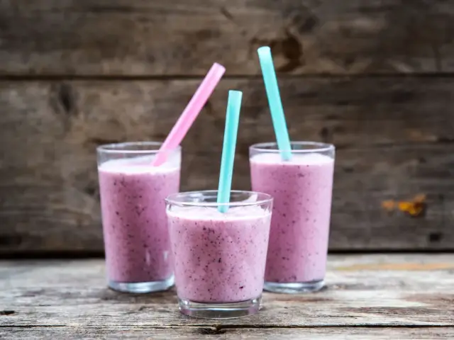 Tre glas med lila smoothie, perfekta för ett snabbt smoothie recept. Blå och rosa sugrör sticker upp.
