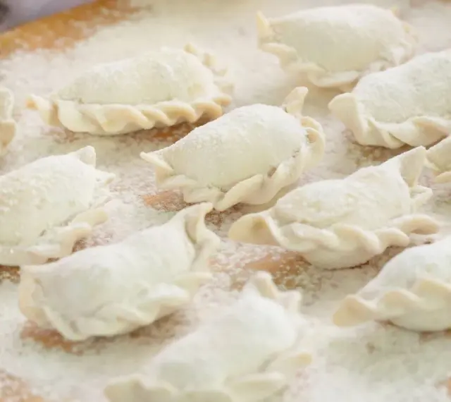 Surowe pierogi, gotowe do gotowania, posypane mąką. Wyglądają jak najlepsze ciasto na pierogi, które mama kiedyś robiła.