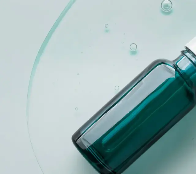 Szklana buteleczka z pipetką, wypełniona zielonym serum, na tle płynu z bąbelkami.