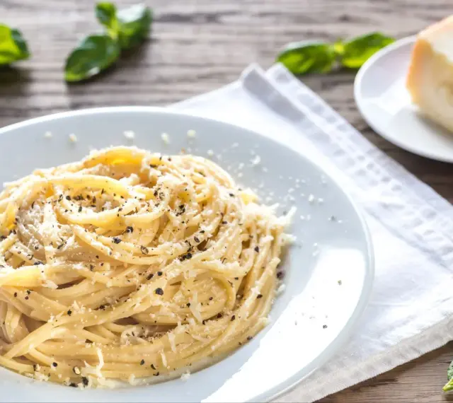 Szybki obiad z makaronem: spaghetti posypane parmezanem i pieprzem, obok kawałek sera i listki bazylii.