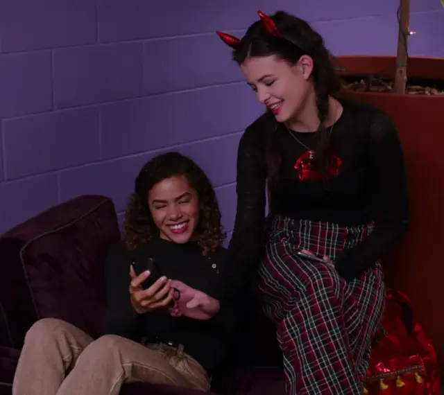 Uśmiechnięte dziewczyny przeglądają telefon, jak pisze zakochana dziewczyna, jedna z nich ma diabelskie rogi.