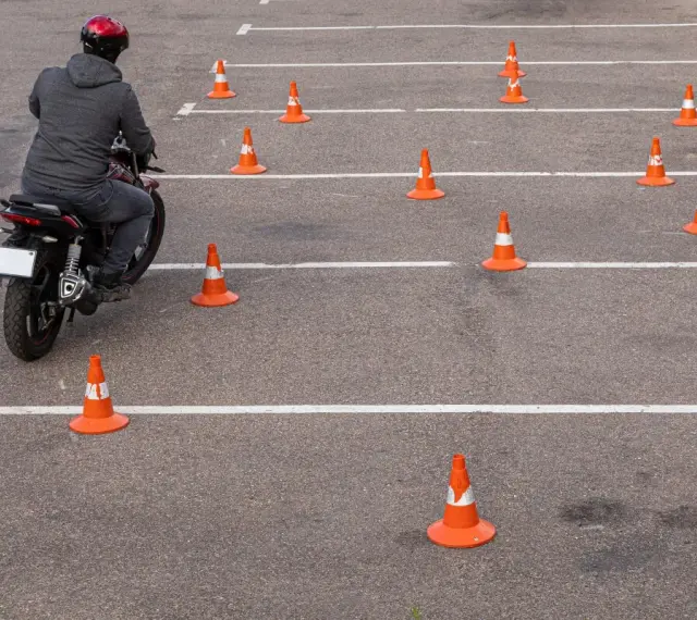 Motocyklista w kasku pokonuje tor przeszkód z pachołków, ćwicząc jazdę na prawo jazdy **kategoria a2**.