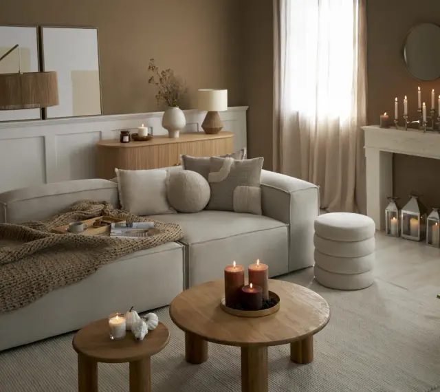 Przytulny salon w odcieniach sepia kolor. Miękki narożnik, drewniane stoliki, kominek z świecami i ciepły pled tworzą atmosferę relaksu.