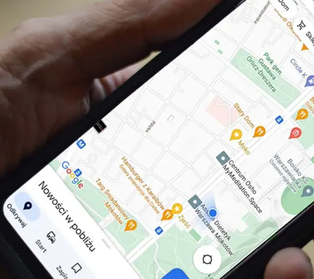 Dłoń trzyma telefon z mapą. Aplikacja do udostępniania lokalizacji pokazuje pobliskie restauracje i sklepy.