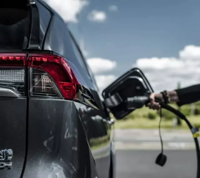 Kobieta podłącza ładowarkę do hybrydowego SUV-a. Zastanawiasz się, ile kosztuje ładowanie elektryka?
