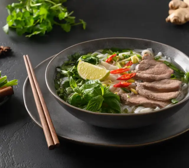 Aromaticzna zupa pho bo z cienko pokrojonym wołowiną, makaronem ryżowym, świeżą miętą, limonką i papryczkami chili.