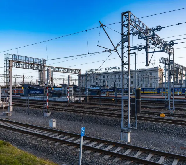 Stacja Gdynia Główna, początek lub koniec najdłuższej trasy kolejowej w Polsce. Tory, perony i budynek dworca pod błękitnym niebem.