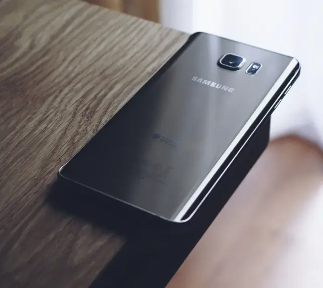 Czarny Samsung leży na drewnianym blacie. Chcesz wiedzieć, jak zresetować telefon Samsung?