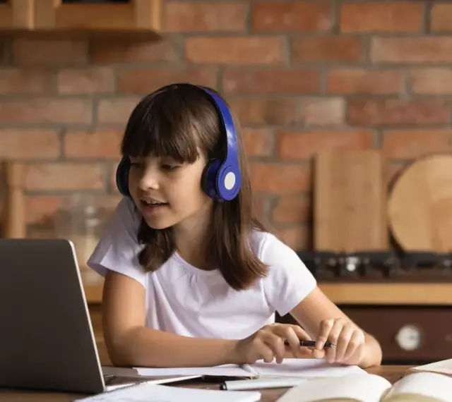 Dziewczynka w słuchawkach uczy się z laptopem. Jej liceum online to przyszłość edukacji.