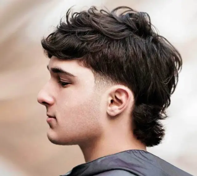 Młody mężczyzna z ciemnymi, kręconymi włosami w nowoczesnej odsłonie fryzury mullet.