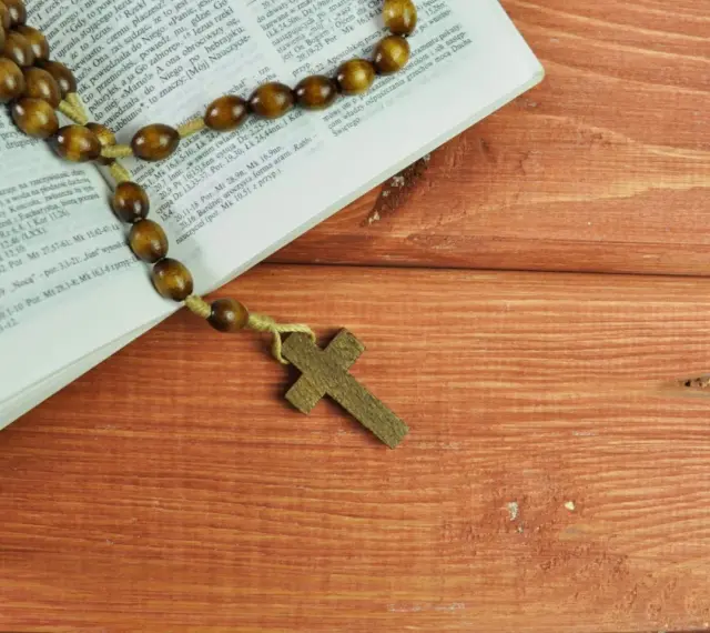 Stary różaniec na drewnianym stole obok Biblii, przypomina o 5 przykazaniach kościelnych.
