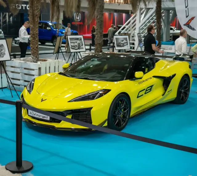 Jaskrawożółty Chevrolet Corvette C8 z czarnym dachem i felgami, prezentowany na niebieskiej podłodze wystawowej.
