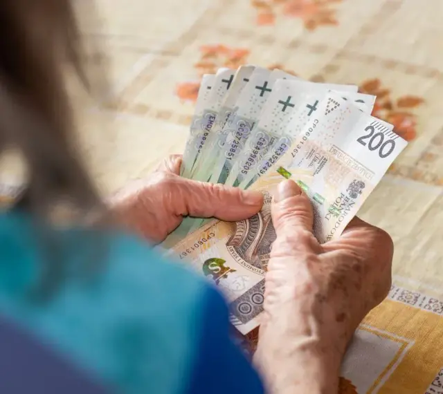 Dłonie starszej osoby liczą banknoty 200 zł. Może to być związane z drugą waloryzacją emerytur, która poprawia byt seniorów.