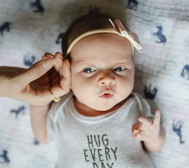 Uroczy 3 tygodniowy noworodek w body z napisem "HUG EVERY DAY", z delikatną opaską na głowie.