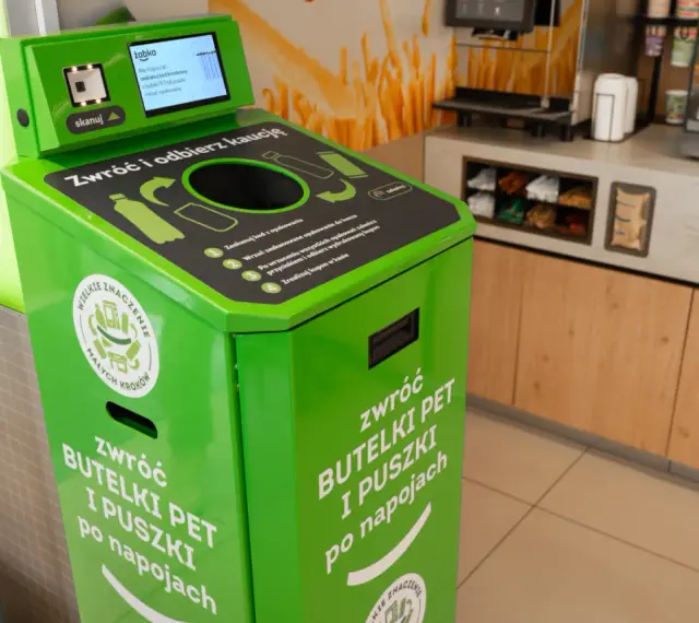 Zielony automat do zwrotu butelek PET i puszek. Skanuj kod, wrzuć opakowanie, by zdjąć zabezpieczenie sklepowe z butelki i otrzymać kaucy.