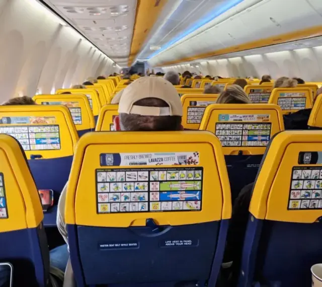 Widok wnętrza samolotu Ryanair z żółtymi oparciami siedzeń i instrukcjami bezpieczeństwa.