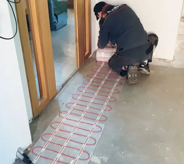 Instalator montuje matę grzewczą, przygotowując ogrzewanie elektryczne podłogi.