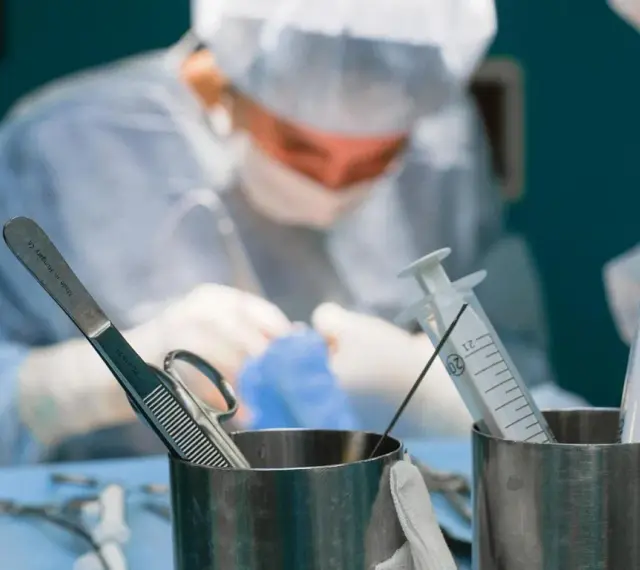 Chirurgowie w akcji. Zastanawiasz się, ile zarabia lekarz? W tle widać zespół medyczny podczas operacji, a na pierwszym planie narzędzia chirurgiczne i strzykawki.