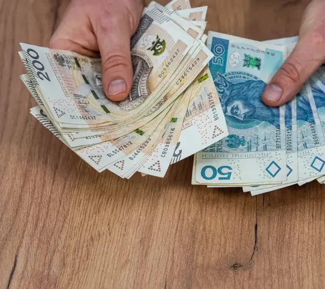 Dłonie trzymające stosy polskich banknotów 200 zł i 50 zł, być może na sześciomiesięczną odprawę emerytalną.