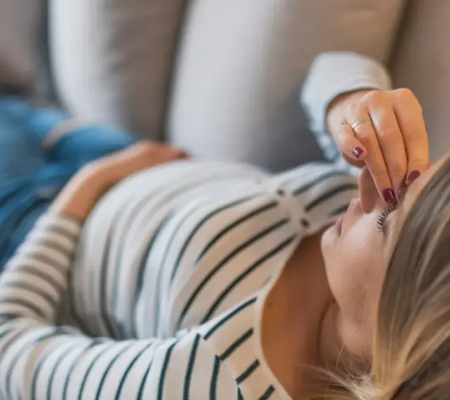 Kobieta w ciąży leży na kanapie, dotykając czoła. Zmartwienie o brak bicia serca w 8 tygodniu ciąży maluje się na jej twarzy.
