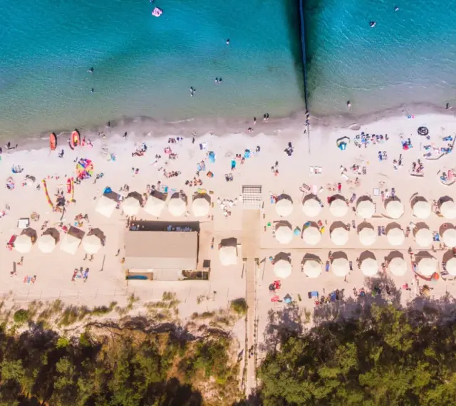 Plaża z parasolami i ludźmi, idealna na wakacje all inclusive Polska.