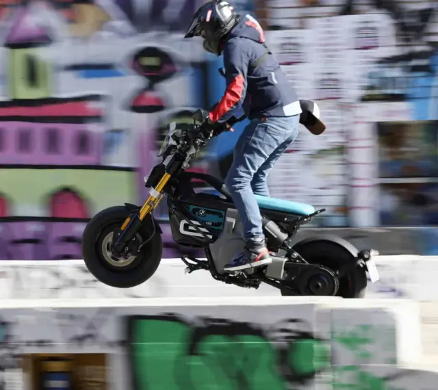 Młody mężczyzna na elektrycznym motocyklu BMW CE02 wykonuje skok na tle kolorowego graffiti.