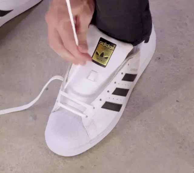 Pokazuję, jak wiązać sznurówki w adidasach Superstar. Białe sznurówki przeplatane przez czarne paski.