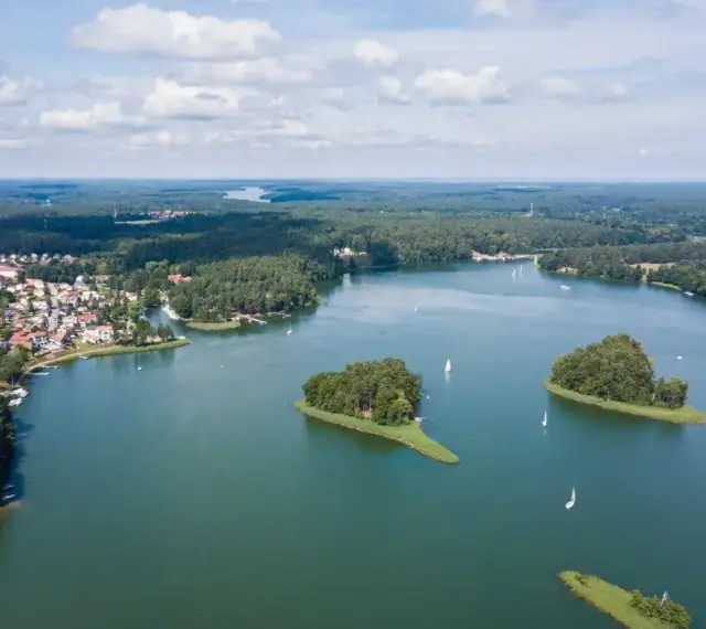 Malownicze jezioro z wyspami i żaglówkami, otoczone lasem i zabudowaniami. To widok, który potwierdza, że to jedne z najpiękniejszych jezior w Polsce.