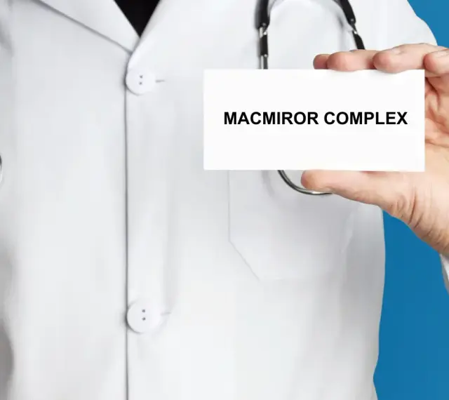 Lekarz w białym kitlu prezentuje kartkę z napisem MACMIROR COMPLEX. Stetoskop wisi na jego szyi.