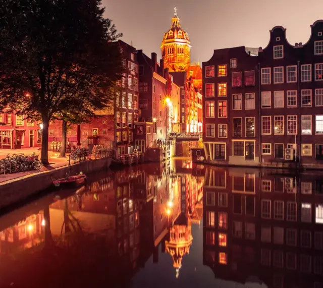 Nocny Amsterdam, kanał odbija oświetlone kamienice i kopułę kościoła. Czerwona ulica Amsterdam w blasku latarni.