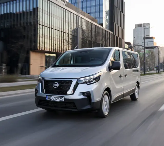 Srebrny van Nissan, jeden z najnowszych nissan modele, jedzie ulicą w nowoczesnym mieście.