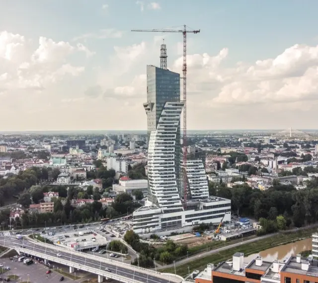 Wielka, kręcona wieża góruje nad miastem. To najwyższy budynek mieszkalny w Polsce, wciąż w budowie, z dźwigiem na szczycie.