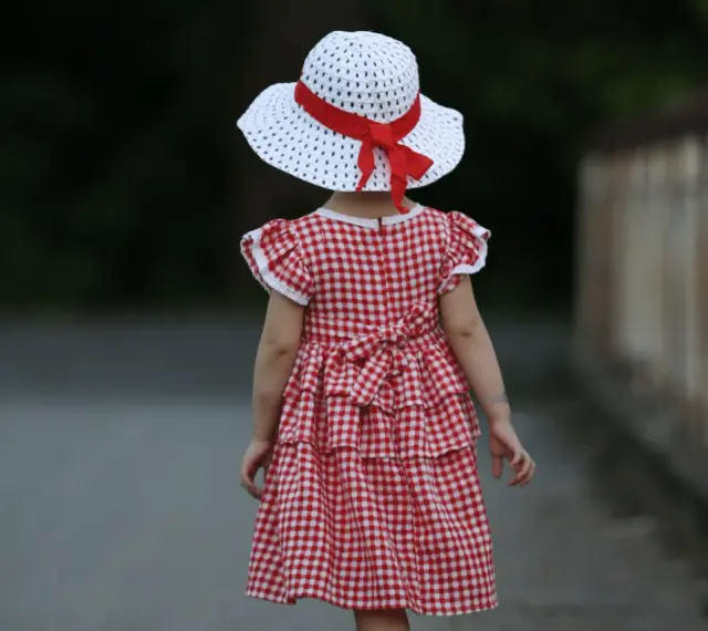 Dziewczynka w sukience w kratkę i kapeluszu z czerwoną wstążką, styl inspirowany modą lat 60.