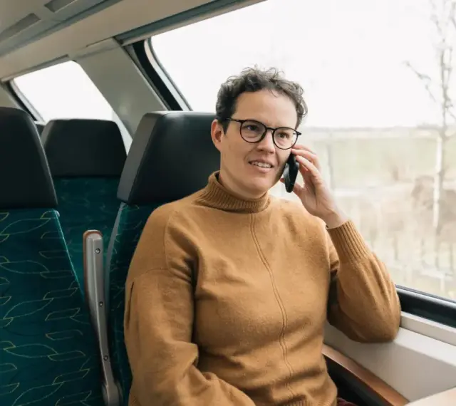 Kobieta w brązowym swetrze rozmawia przez telefon w pociągu. Czas na moją kolej, by usiąść przy oknie i podziwiać widoki.