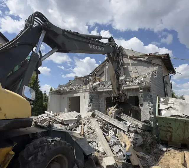 Koparka Volvo niszczy budynek. Trwa rozbiórka budynku, cena za m2 jest kluczowa przy planowaniu prac.