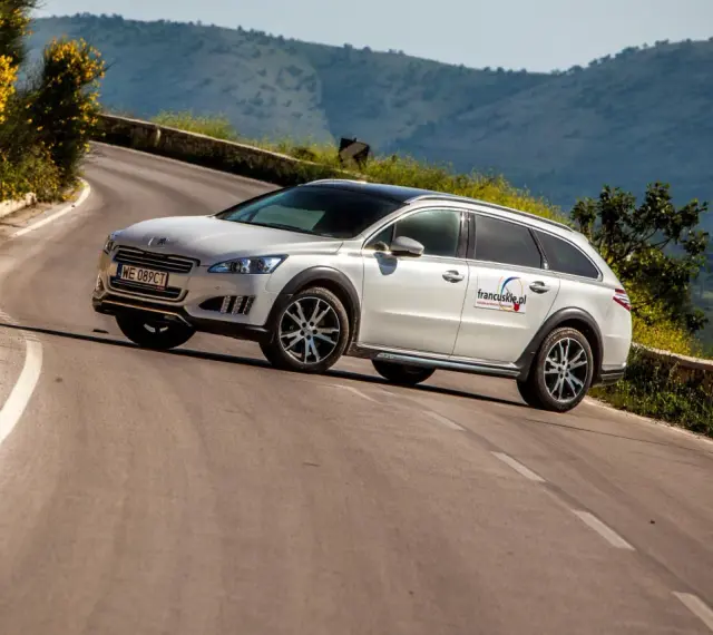 Białe kombi Peugeot 508 RXH na krętej drodze w górach.