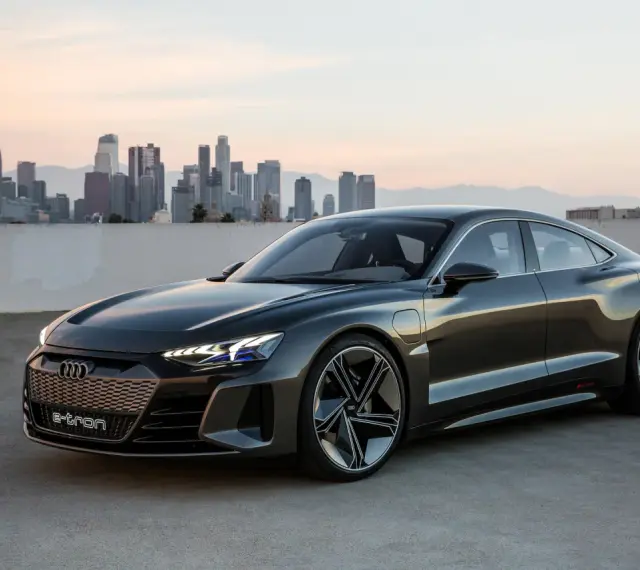 Ciemnoszary Audi e-tron GT stoi na tle panoramy miasta o zachodzie słońca.