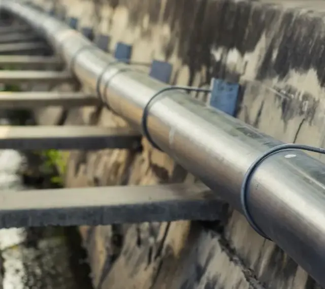 Metalowa rura biegnie wzdłuż betonowego koryta. To element kanalizacji ciśnieniowej, transportującej wodę.
