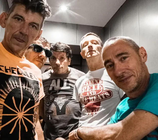 Cinq hommes aux têtes brûlantes, certains souriants, d'autres plus intenses, posent pour un selfie. Leurs t-shirts affichent des graphismes variés.