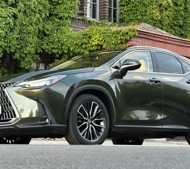 Ciemnozielony Lexus NX 450h+ plug-in zaparkowany przed budynkiem porośniętym bluszczem.