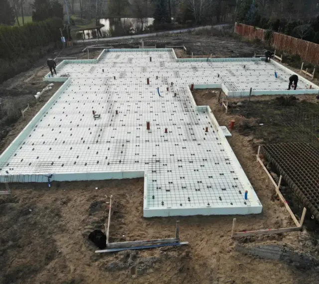 Budowa domu: przygotowane słupy fundamentowe, zbrojenie i izolacja płyty fundamentowej.