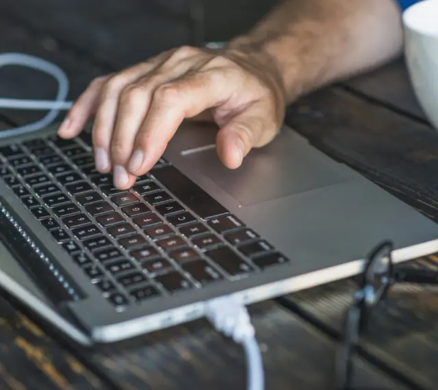 Dłoń na klawiaturze laptopa, przygotowująca się do twardego resetu. Obok biały kubek.