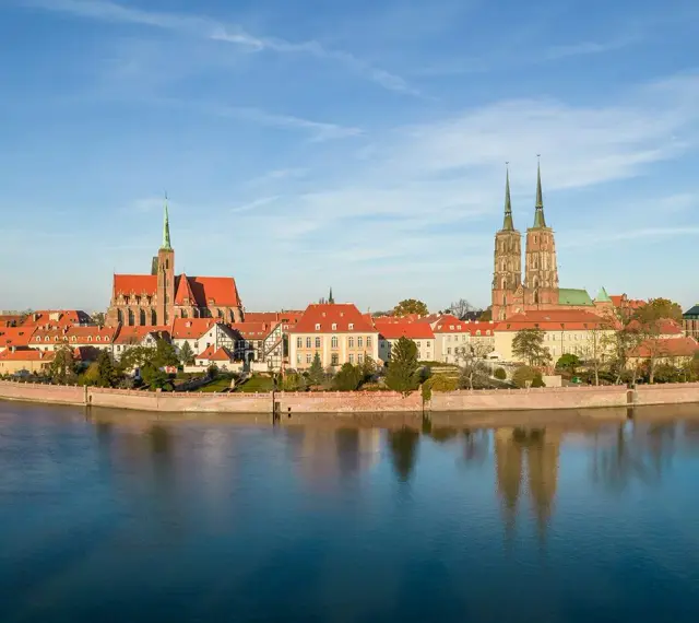 Widok na Ostrów Tumski we Wrocławiu z rzeką i odbiciem budynków w wodzie.