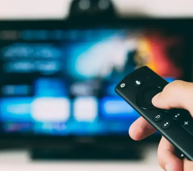 Dłoń trzymająca pilot do telewizora LG, ekran pokazuje menu. Dowiedz się, jak wyłączyć lektora w telewizorze LG.
