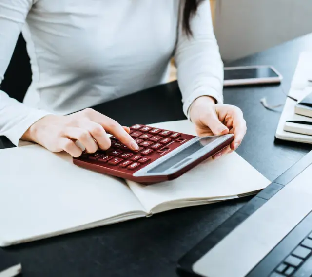 Kobieta liczy wydatki na własne cele mieszkaniowe, przygotowując PIT-39. Na biurku notatnik, kalkulator i laptop.